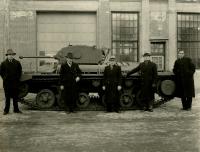 Photograph outside of a manufacturing site of Valentine tanks in Montreal. The picture shows a Valentine tank behind four men dressed for cold weather. Black and white photograph. 
